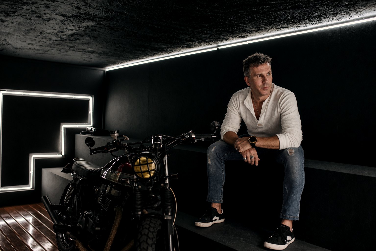 Chris Kypriotis seated beside a motorcycle in a dark studio